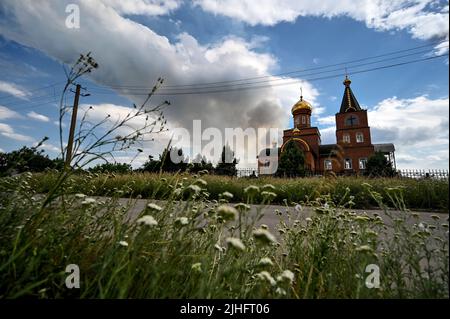 ZAPORIZHZHIA REGIONE, UCRAINA - 17 LUGLIO 2022 - Un plume di fumo visto da dietro una chiesa sorge sopra un campo di grano ardente come le truppe russe conchiglia fi Foto Stock