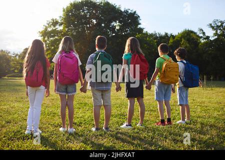 Bambini con zaini sulle spalle, mani in mano, stare in fila nel parco. Foto Stock