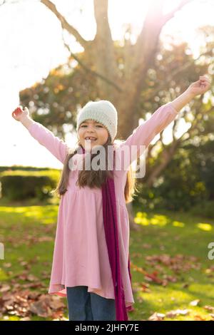 Immagine verticale di felice ragazza caucasica che gioca con foglie d'autunno in giardino Foto Stock