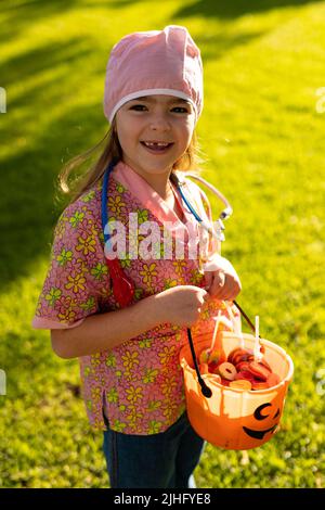 Immagine verticale di felice ragazza caucasica in costume medico in autunno giardino Foto Stock