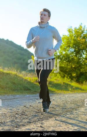L'uomo che fa jogging nella natura rurale durante la splendida giornata estiva. Sport fitness modello caucasico etnia formazione all'aperto. Foto Stock