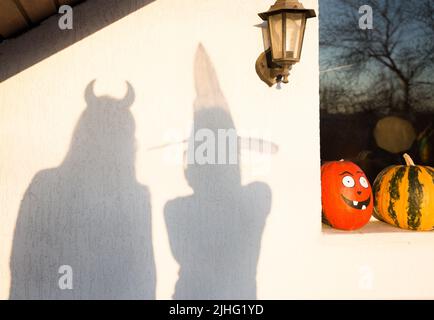 Su una parete di luce, due ombre di sagome di persone in costumi festosi, preparandosi per una festa di Halloween. Street decor, zucche dipinte al vento Foto Stock