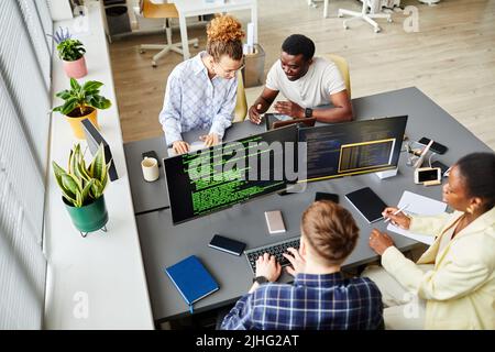 Visualizzazione ad angolo elevato dei programmatori seduti al tavolo con monitor per computer e scrittura di codici in team in ufficio Foto Stock