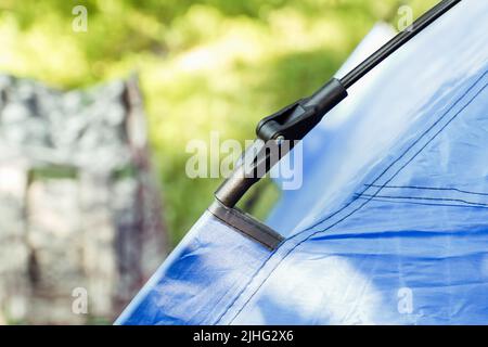 Defocus closeup tenda turistica blu in piedi su sfondo verde natura. Zaino militare. Concetto di turismo. Vacanze estive nella foresta, campeggio. Cacciatore Foto Stock
