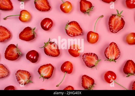 Sfondo di fragole e ciliegie mature su sfondo rosa.trendy, fruttato, sfondo estivo. Foto Stock
