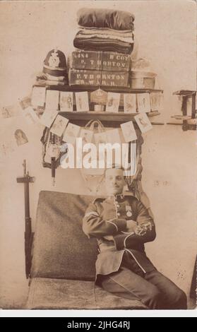 Philip Thornton, Royal Warwickshire Regiment, ha fotografato nel suo spazio letto caserma a Portland. Thornton è in uniforme, con una medaglia, e ha il suo casco da esercito, asciugamani o biancheria da letto, e le casse sugli scaffali dietro di lui. Il suo fucile è sul muro a sinistra del letto e cartoline e foto (la maggior parte con un tema militare) sono appese agli scaffali. Questa cartolina fotografica è stata inviata alla sua futura moglie Hilda White nel 1905. Thornton è stato ucciso in Francia il 13 ottobre 1914, all'età di 33 anni, durante i primi mesi della prima guerra mondiale Foto Stock