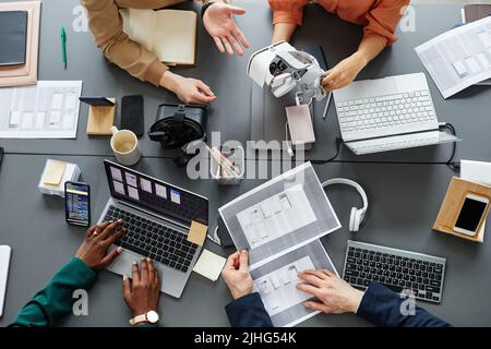 Vista ad alto angolo del team di sviluppatori che testa la nuova applicazione per occhiali per realtà virtuale al tavolo durante una riunione Foto Stock