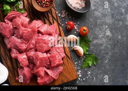 Carne di manzo tritata cruda. Carne bovina biologica cruda o agnello, spezie, erbe su vecchio asse di legno su sfondo di cemento grigio scuro. Goulash. Carne cruda non cotta. Foto Stock