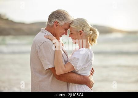 Primo piano di una coppia caucasica anziana felice in piedi e abbracciarsi l'un l'altro in una giornata fuori alla spiaggia. Marito e moglie maturi sorridendo e mostrando Foto Stock
