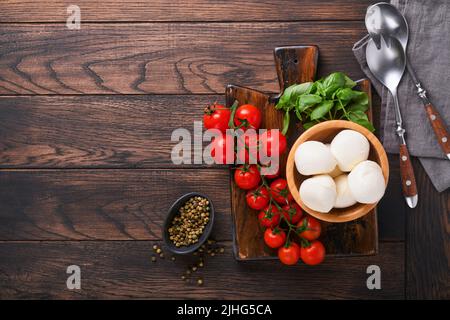 Insalata caprese, ingredienti per la cottura. Taglio del legno con preparazione caprese tradizionali: Mozzarella, pomodori, basilico, olio d'oliva Foto Stock