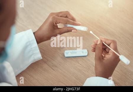 Mani di un medico che tiene un test covid e un campione di tampone. Primo piano sulle mani di un medico afroamericano utilizzando un test del virus corona. Tenuta gp dedicata Foto Stock