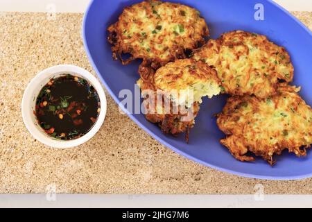 Frittelle di zucchine, frittelle di zucchine vegetariane su un piatto ovale blu servito con salsa di soia in un piccolo recipiente bianco. Cibo vegetariano Foto Stock