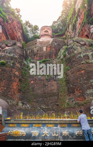 Leshan, Cina - Luglio 2019 : candele cinesi maschili per il pellegrino che illuminano il monumento in fondo al Buddha gigante di Leshan, una statua di pietra alta 71 metri Foto Stock