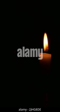 Immagine verticale di candela e fiamma incandescente su sfondo nero Foto Stock