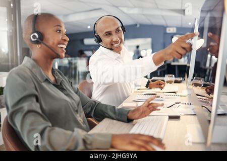 Agente di telemarketing maschile di razza mista che discute i piani con un collega mentre lavora insieme al computer in un ufficio. Due consulenti Foto Stock