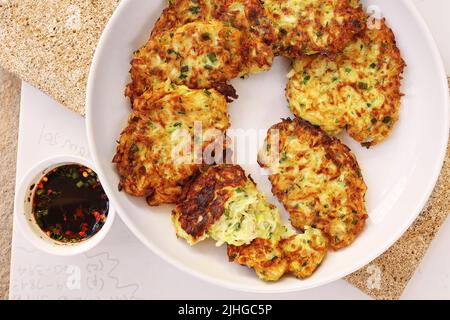 Frittelle di zucchine, frittelle di zucchine vegetariane su un piatto bianco servito con salsa di soia in un piccolo recipiente bianco. Cibo vegetariano Foto Stock