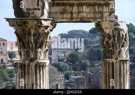 Guardando verso l'arco di Tito attraverso le colonne corinzie del Tempio di Vespasiano e Tito nel Foro Romano, Roma Centrale, Lazio, Italia. Foto Stock