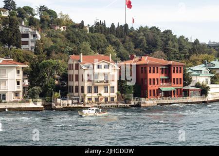 Vista di una piccola barca da pesca sul Bosforo e palazzi storici e tradizionali nella zona di Kandilli del lato asiatico di Istanbul. È una giornata estiva soleggiata Foto Stock