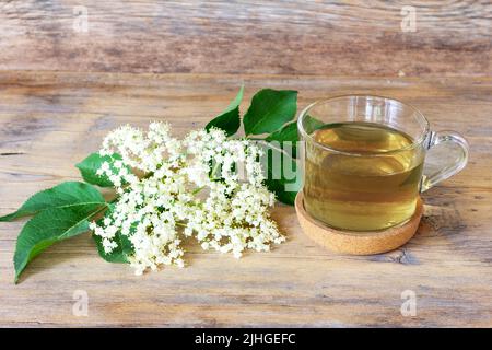 sambuco bere in una tazza su uno sfondo di legno con un rametto di fiore sambuco primo piano Foto Stock