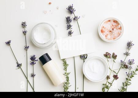 Mockup biglietto da visita. Crema per la pelle, idratante e shampoo in bottiglia. Erbe di lavanda, origano e satureja con sale di Himalaya. Sfondo bianco della tabella Foto Stock