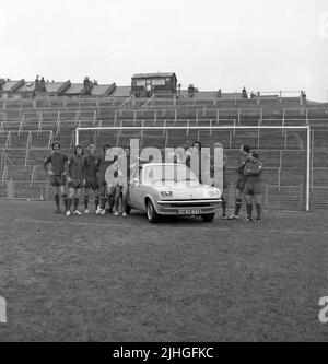 1974, storico, football manager, Malcolm Allison seduto in berlina Chevette a 2 porte in campo al Selhurst Park, con giocatori di squadra in piedi intorno. Selhurst Park è la sede del Crystal Palace Football Club. Una capanna di legno sulla cima di ripide terrazze a scoscesa dice Police Post. Foto Stock