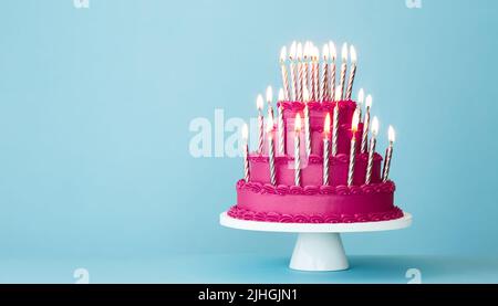 Stravagante torta di compleanno a più livelli rosa con un sacco di candele di compleanno oro su sfondo blu Foto Stock