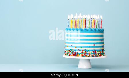 Torta di compleanno a strisce con candele di compleanno colorate e spolverate su sfondo blu Foto Stock