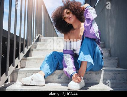 Giovane donna da corsa mista alla moda con occhiali curly afro che si godono una giornata fuori in città nel fine settimana. Una donna ispanica sicura ed elegante Foto Stock