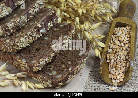 Pane nero con semi di sesamo e semi di girasole, pikelets di avena e grani di grano in un cucchiaio di legno Foto Stock