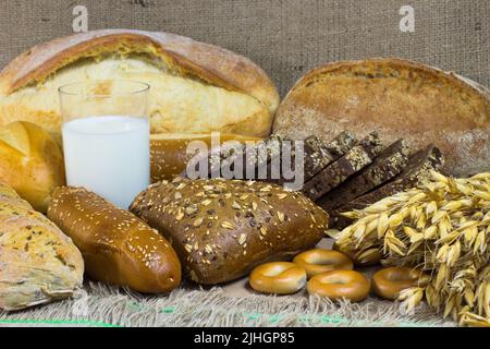 Pane bianco e nero, baguette, panna, un mazzo di avena, un bicchiere di latte sul sacco Foto Stock