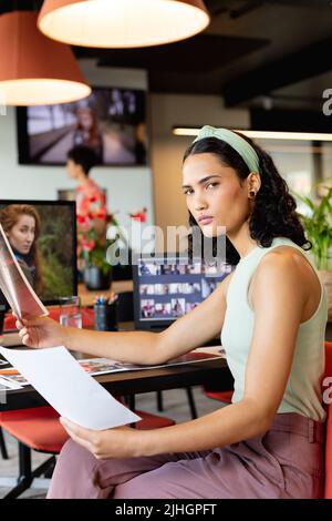 Ritratto di fidata giovane donna d'affari biraciale con fotografie al banco in ufficio Foto Stock
