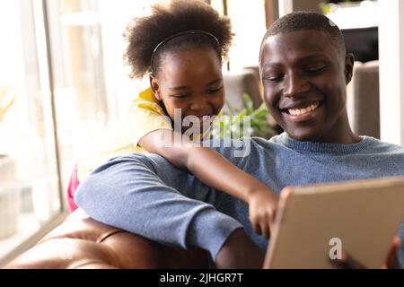 Immagine di felice padre e figlia afroamericana seduto sul divano con tavoletta Foto Stock