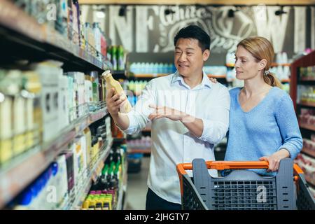 Gli acquirenti felici uomo e donna asiatici comprare e scegliere le merci in supermercato, shopping di famiglia Foto Stock