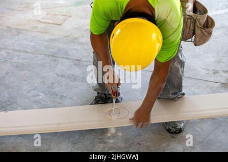 drywaller sta tagliando fuori un foro per un'uscita di tubo su un pezzo di drywall che sarà installato contro il muro di un appartamento residenziale parete. Foto Stock