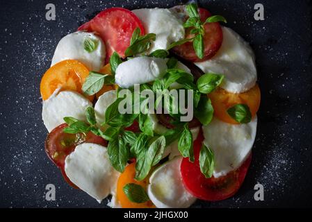 Insalata di caprese fresca fatta in casa su un piatto nero di ardesia. Mozzarella, basilico e tre tipi di pomodori. Cucina italiana. Antipasto. Vista dall'alto. Disposizione piatta. Foto Stock