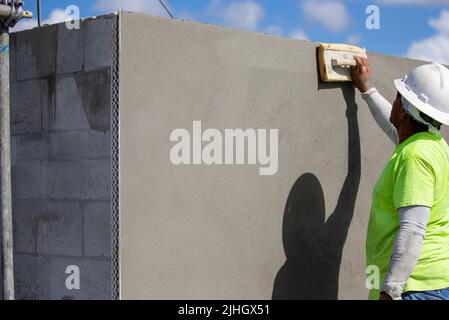 Un operaio di costruzione sta usando una cazzuola della spugna per lisciare fuori il rivestimento finale di un'applicazione dello stucco ad una parete esterna su un edificio multiplex Foto Stock