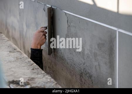 Lavoratore di costruzione che applica fango di stucco all'esterno di un edificio multiplex in costruzione. Dimora Multi Story con impalcatura Foto Stock