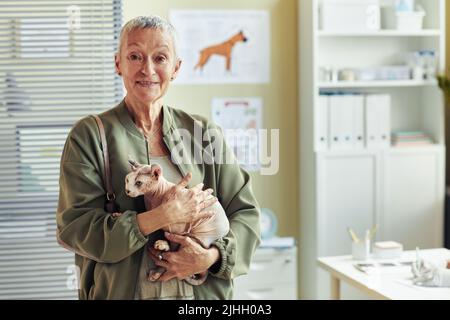 Vita su ritratto di sorridente donna anziana che tiene gatto senza capelli in clinica di veterinario al controllo di salute dell'animale domestico in su, spazio di copia Foto Stock