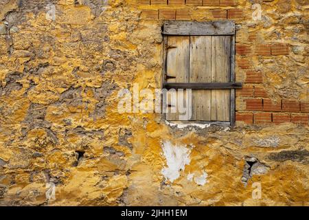 Vecchio cracked tempo shabby giallo dipinto intonacato pelato e sfondo muro di mattoni. La finestra di legno. Foto Stock