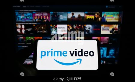 Persona che tiene lo smartphone con il logo del servizio di streaming Amazon prime Video sullo schermo di fronte al sito Web. Mettere a fuoco sul display del telefono. Foto Stock