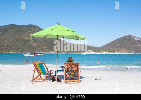 Uomo con cappello da sole su lettini colorati accanto all'ombrello, sulle spiagge paradisiache di Pontal do Atalaia Cabo Frio, Brasile. Foto Stock