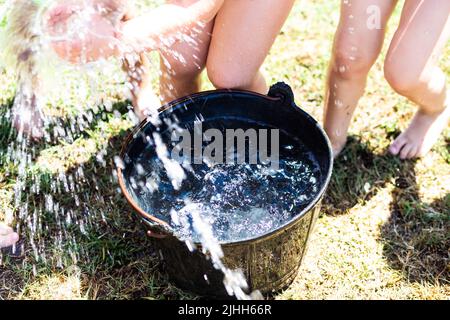 Secchio di plastica nera con acqua dolce con molti bambini gambe giocare giochi estivi su un prato verde erba Foto Stock