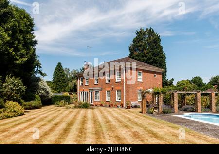 Esterno di una casa indipendente, giardino sul retro e piscina, il prato con strisce ma marrone da siccità e temperature calde in estate, Surrey, Regno Unito Foto Stock