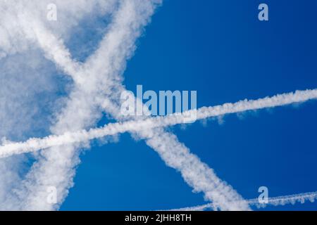 Velivoli bianchi percorsi vapore e nuvole contro un cielo blu in una giornata di sole in estate a Surrey, nel sud-est dell'Inghilterra dai voli dell'aeroporto di Heathrow Foto Stock