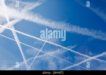 Velivoli bianchi percorsi vapore e nuvole contro un cielo blu in una giornata di sole in estate a Surrey, nel sud-est dell'Inghilterra dai voli dell'aeroporto di Heathrow Foto Stock