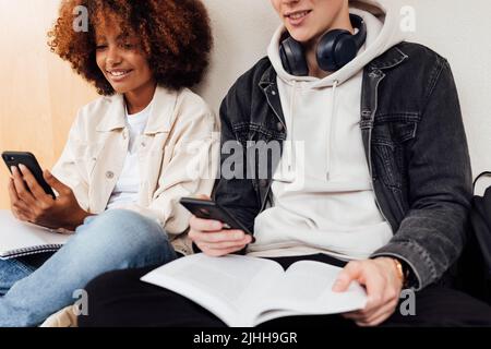 Scatto ritagliato di due studenti universitari che leggono dagli smartphone durante la preparazione degli esami Foto Stock