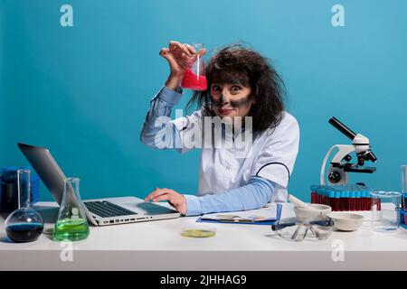 Stupido e divertente chemist che ha matraccio di vetro riempito con siero liquido sperimentale dopo esperimento chimico fallito. MAD silly lavoratore di laboratorio con aspetto selvaggio e strana espressione del volto. Foto Stock