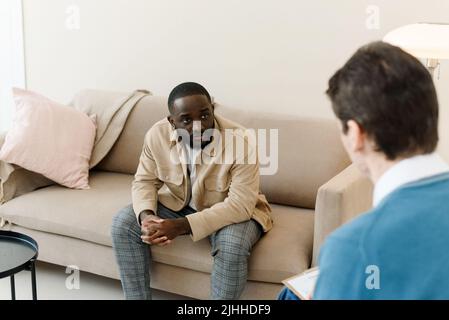 Infelice giovane uomo nero che ha una sessione con lo psicologo professionista alla clinica di salute mentale. Concetto di aiuto psicologico professionale Foto Stock