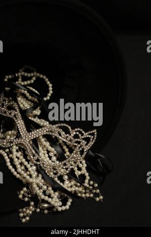 Un mucchio di varie collane di perle da vicino e su uno sfondo neutro con elementi aggiuntivi come un vaso, vecchio cappello, maschera, e canister rosso/oro di stoccaggio. Foto Stock