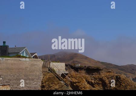 La nebbia costiera che si affaccia sulle colline pedemontane attraverso la superstrada da una spiaggia pubblica a Cayucos, CA. Una casa in affitto con accesso alla spiaggia si trova sulla scogliera. Foto Stock